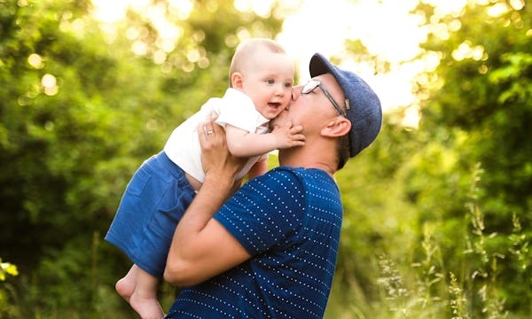 Father holding baby up infront of lush green woodland